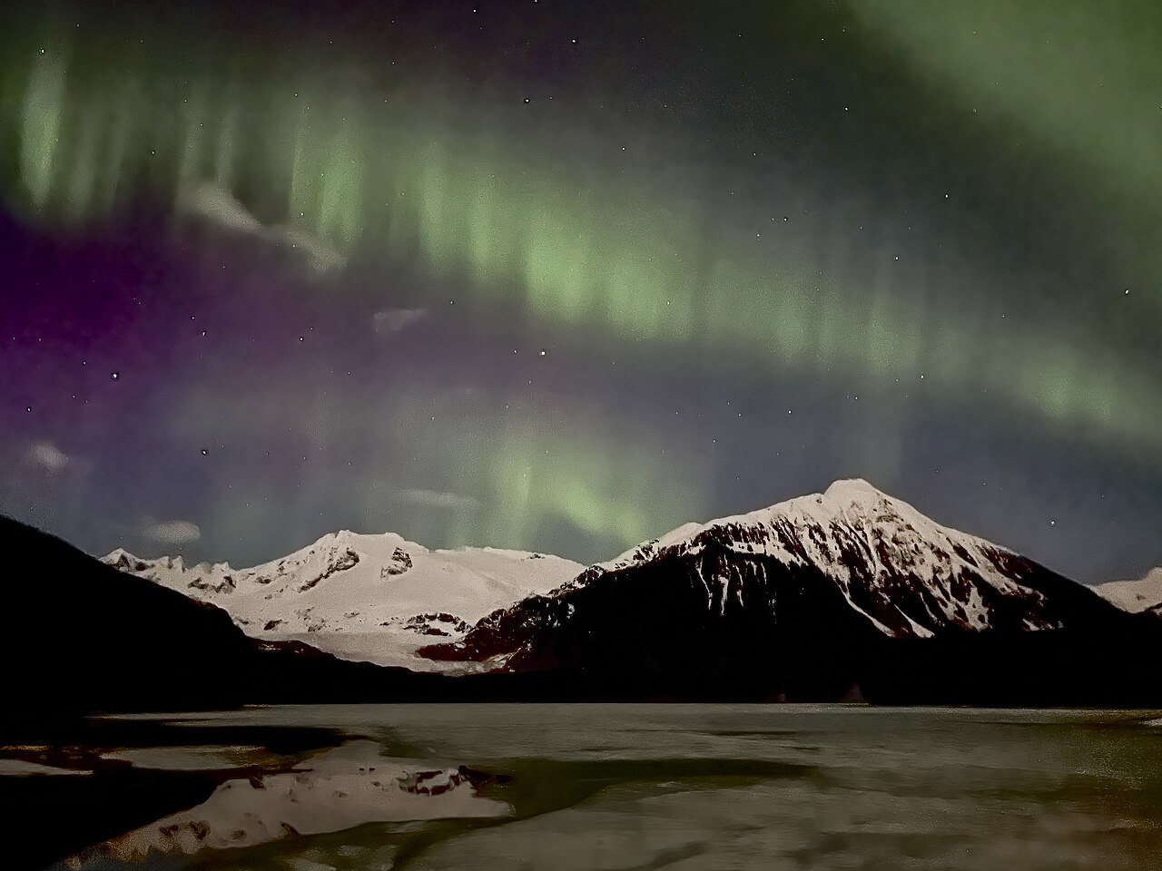 Green and purple aurora borealis glowing over a snowy mountain landscape at night