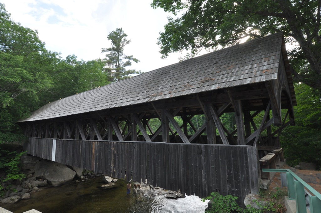 The historic Sunday River covered bridge near Bethel, Maine, surrounded by summer forest