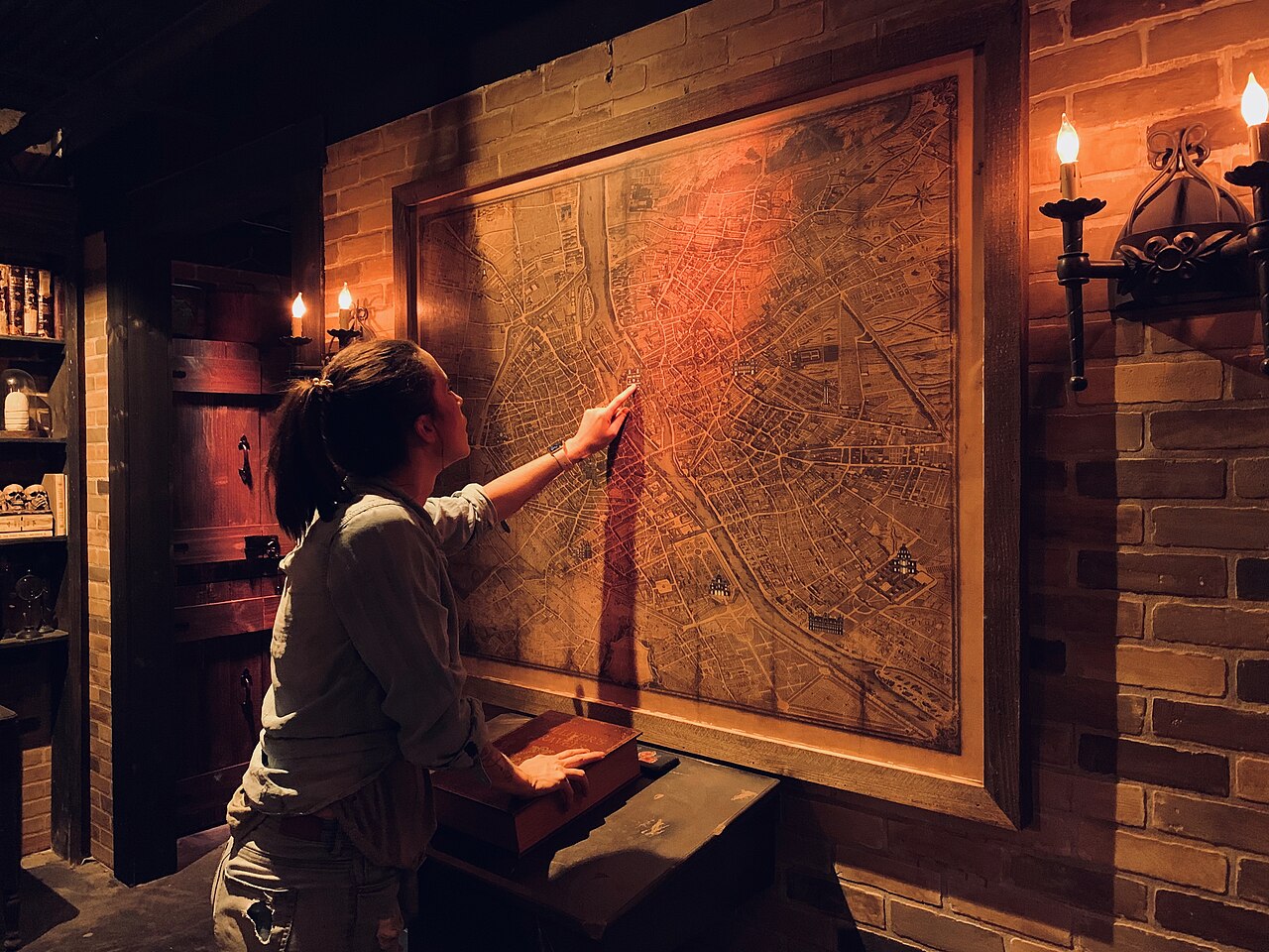 Inside an atmospheric escape room, a player studies an antique map by candlelight
