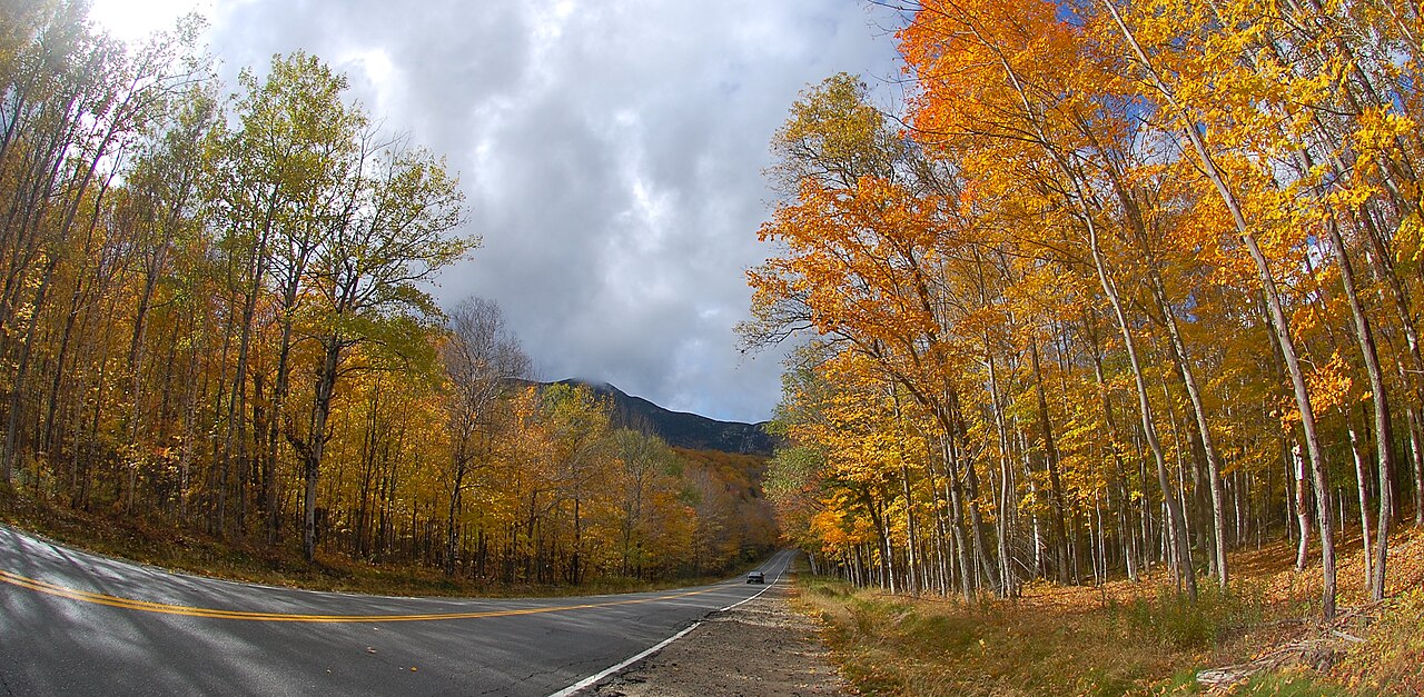 A road winding through brilliant orange and gold autumn foliage in Grafton Notch, Maine